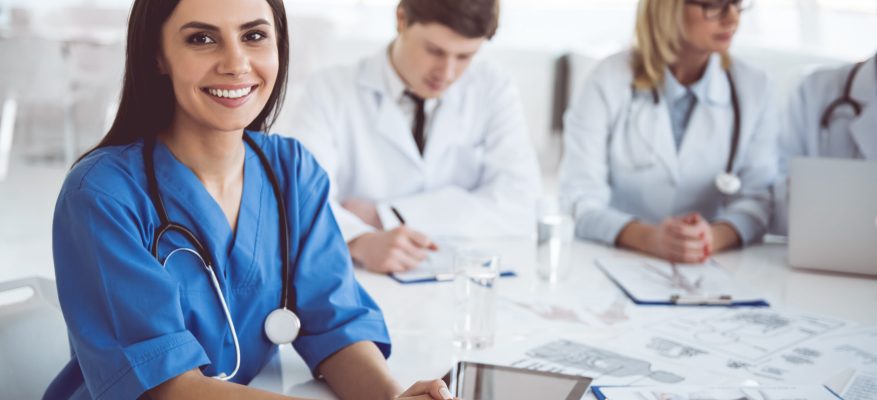 Successful medical doctors are sitting at the conference. Beautiful young female doctor is looking at camera and smiling